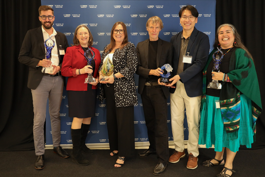 Six 2026 award winners pose in front of the UC Davis Health School of Medicine step-and-repeat